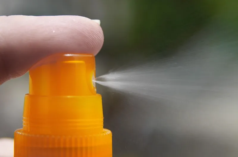 A hand using a fine mist spray bottle to gently moisten the surface of seed starting soil